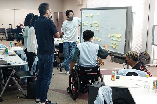 社内ホールで研修中の社員と一緒にホワイトボードの前でワークショップを行っている様子