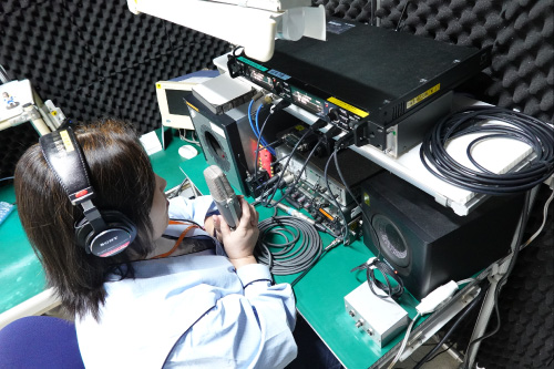 女性社員がヘッドホンを装着しC-38Bマイクの音響検査を行っている様子