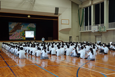 学校の講堂で生徒たちを前に講演を行っている社員