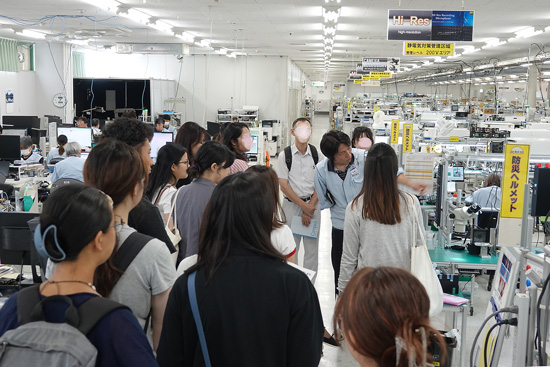 会社見学のグループに製造作業の様子を見ながら説明している社員