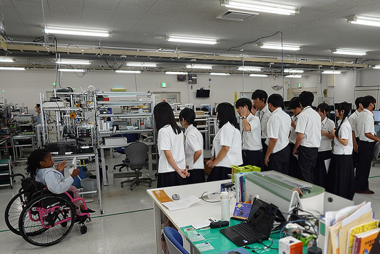 高校生が工場見学で弊社の車いす社員から説明を受けている様子